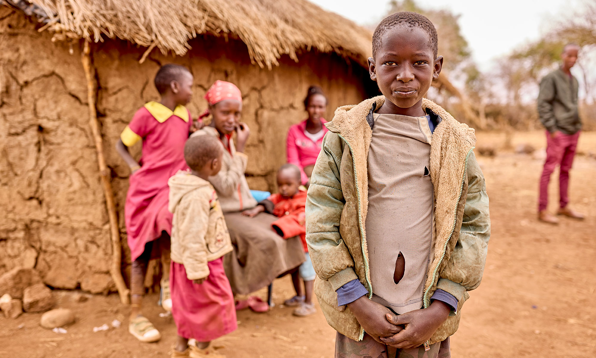 A young Maasai boy standing outside his family home