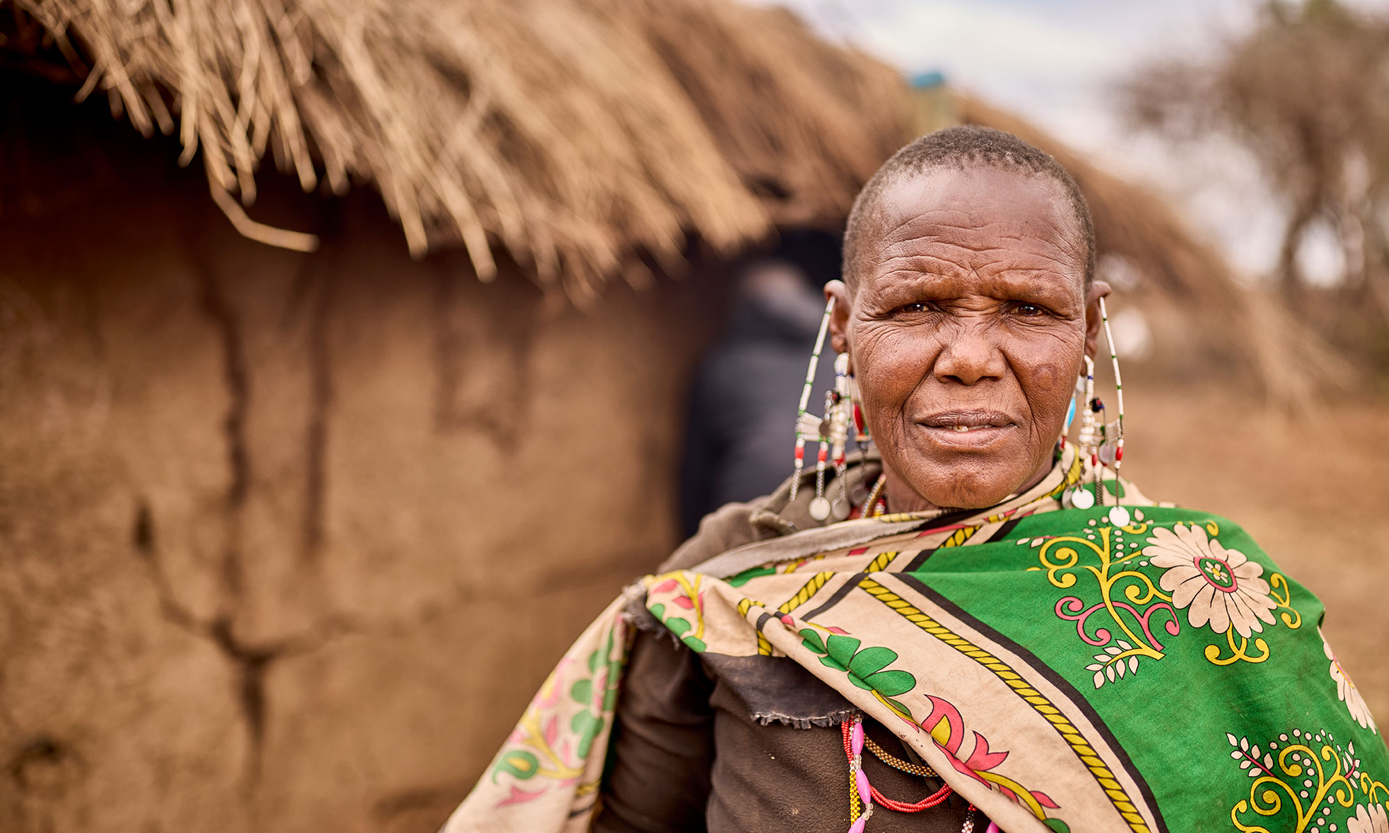 A Maasai woman wearing a green patterned wrap and traditional beaded jewelry